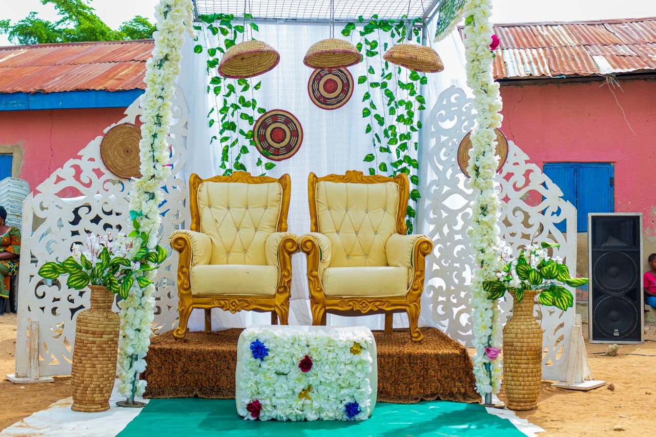 Charming wedding seating area with ornate chairs, floral decorations, and rustic backdrop.